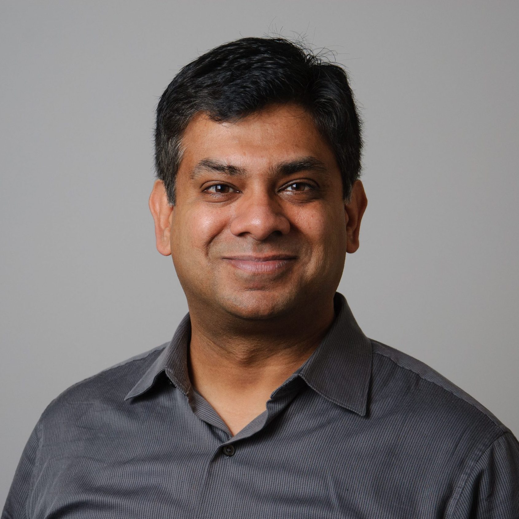 Professional headshot of a smiling individual wearing a dark button-down shirt, posed against a neutral background.