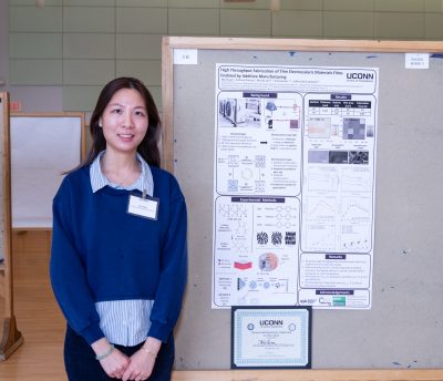 Person standing next to a research poster display at an academic event, with charts and diagrams visible on the board.