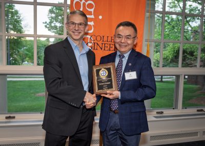 Two men stand together at a UConn College of Engineering event, holding an Academy of Distinguished Engineers plaque.